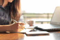Business woman using laptop and writing on a notepad with a pen at a coffee shop. Working on project concept