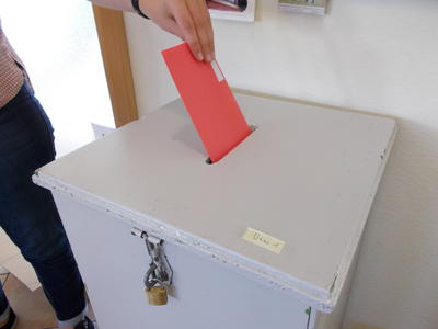 Eine Person l�sst einen roten Umschlag in einen verschlossenen Wahlbeh�lter fallen.