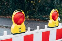 Rote-wei�e Absperrbake mit zwei gelben Warnleuchten vor Stra�enrand und B�schen