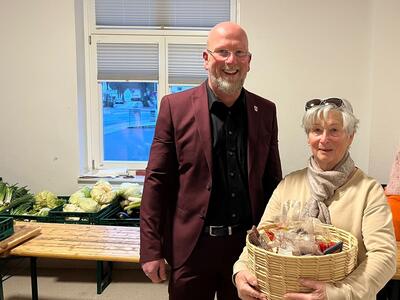 B�rgermeister Marko Steiner steht neben Ingrid Ramm, die einen Geschenkkorb in der Hand h�lt.