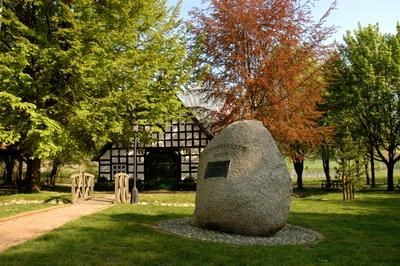 Zu sehen ist das Haus der Begegnung an einem Tag im Fr�hling. Die Bl�tter der B�ume erstrahlen in vielen verschiedenen Farben. Das Haus ist ein altes Fachwerkhaus und vor dem Haus steht ein gro�er Stein auf dem etwas steht.