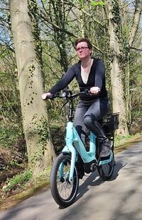 Das Bild zeigt eine Radfahrerin auf einem E-Bike, die durch eine Allee im Kurpark von Bad Holzhausen f�hrt.