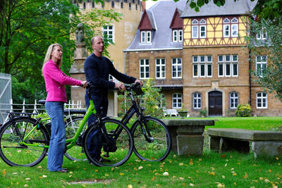 Zusehen ist ein Mann und eine Frau, die mit ihrem Fahrrad in der Natur stehen und sich etwas anschauen.